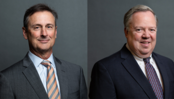 Two Middle-aged Men In Business Suits Pose For Professional Headshots Against A Plain Gray Background. The Man On The Left Wears A Striped Tie, And The Man On The Right Wears A Patterned Tie. Both Are Smiling Slightly.