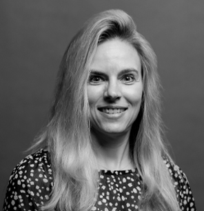 Black and white portrait of a smiling woman with long, light-colored hair, wearing a patterned blouse, set against a plain background.