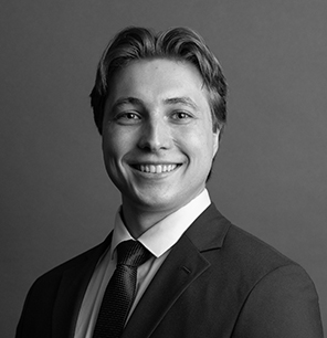 Black and white portrait of a man in a suit and tie, smiling at the camera with a neutral gray background.