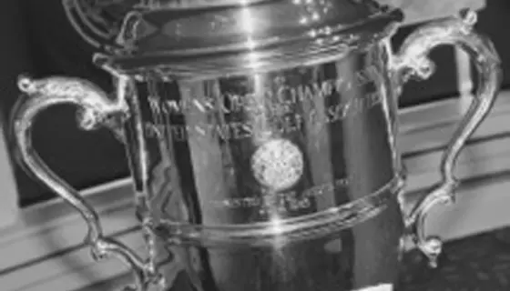 A close-up of a silver trophy cup with ornate handles and engraved text, displayed indoors. The text mentions a championship and the United States. The image is in black and white.
